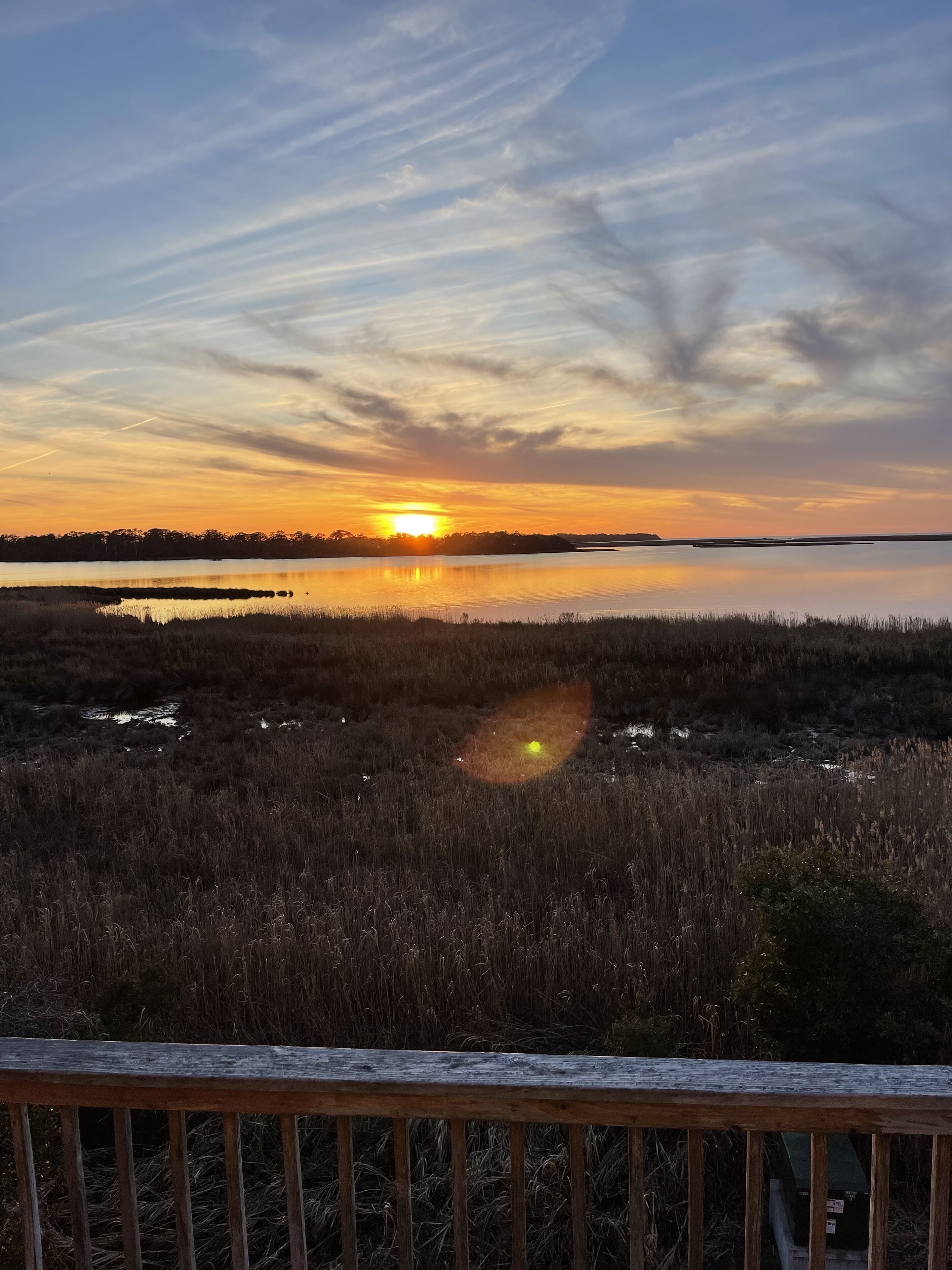 A sunset over a calm lake with a wooden deck in the foreground.