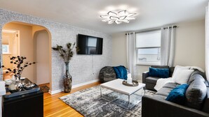 A modern living room with a white brick wall, a flat-screen TV mounted above a sofa, and a wooden floor. - Christmas City Cottage (Bethlehem)