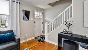 A modern living room with a grey sofa, a staircase, and a desk with decorative items. - Christmas City Cottage (Bethlehem)