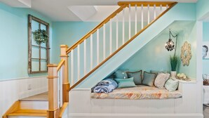 A staircase with wooden handrails and a white banister, leading to a seating area with a floral-patterned sofa and cushions.