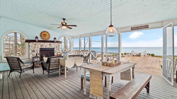 A covered outdoor area with a stone fireplace, wicker furniture, and a view of the beach.