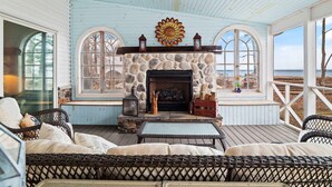 A cozy room with a stone fireplace, wicker furniture, and large windows overlooking the beach.