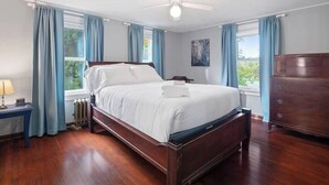 Un dormitorio con cama de madera, ventilador de techo, cómoda y ventana con cortinas.