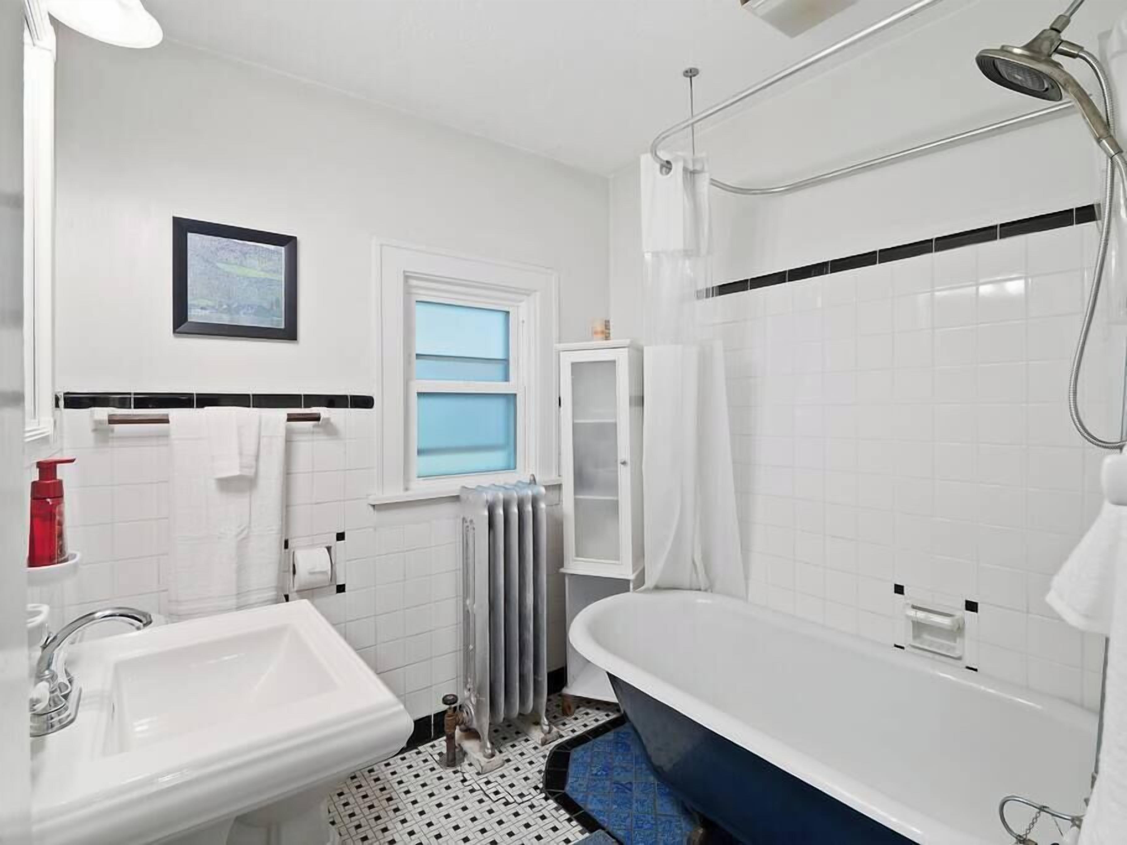 A bathroom with a white sink, a bathtub, a shower, and a window with blue-tinted glass.