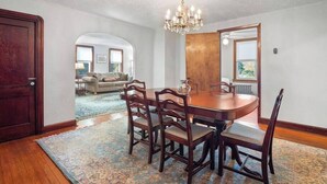 Un comedor con una mesa y sillas de madera, una araña y vista a una sala de estar por un arco.