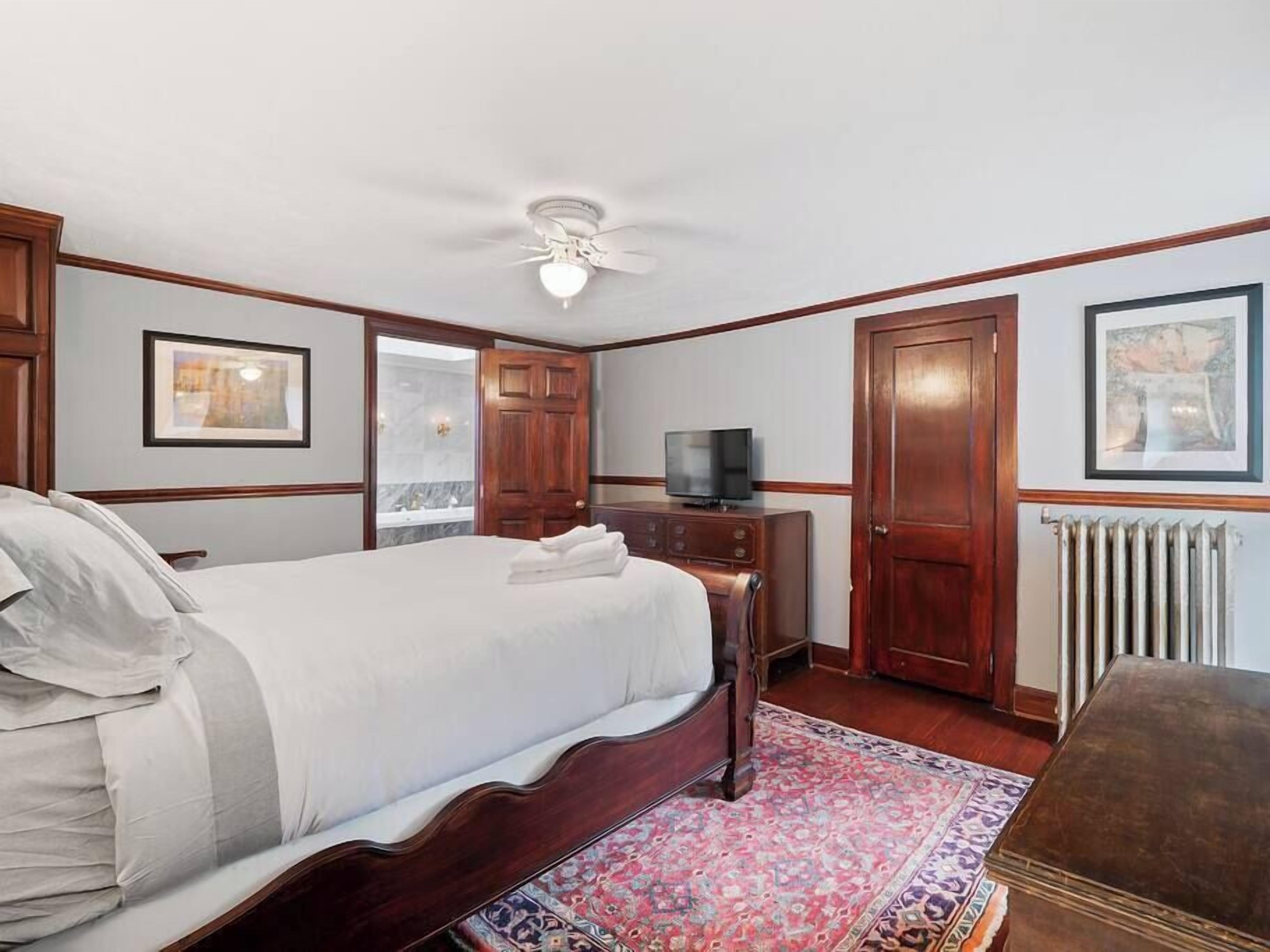 Una camera d'albergo con un letto grande, una televisione, un settimino in legno e un termosifone.