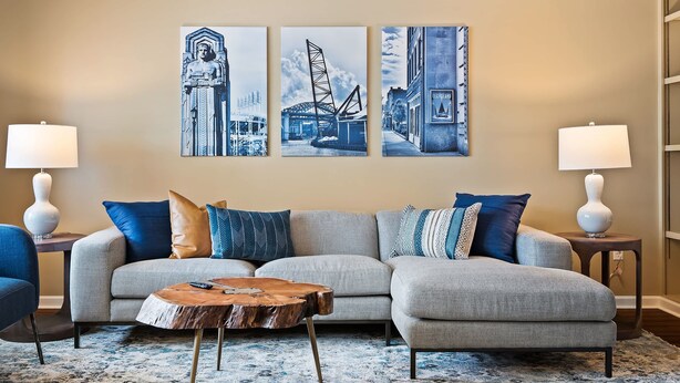 Ein Wohnzimmer mit grauem Sofa, blau-weißen Kissen, einem Holztisch und drei gerahmten Kunstwerken an der Wand.