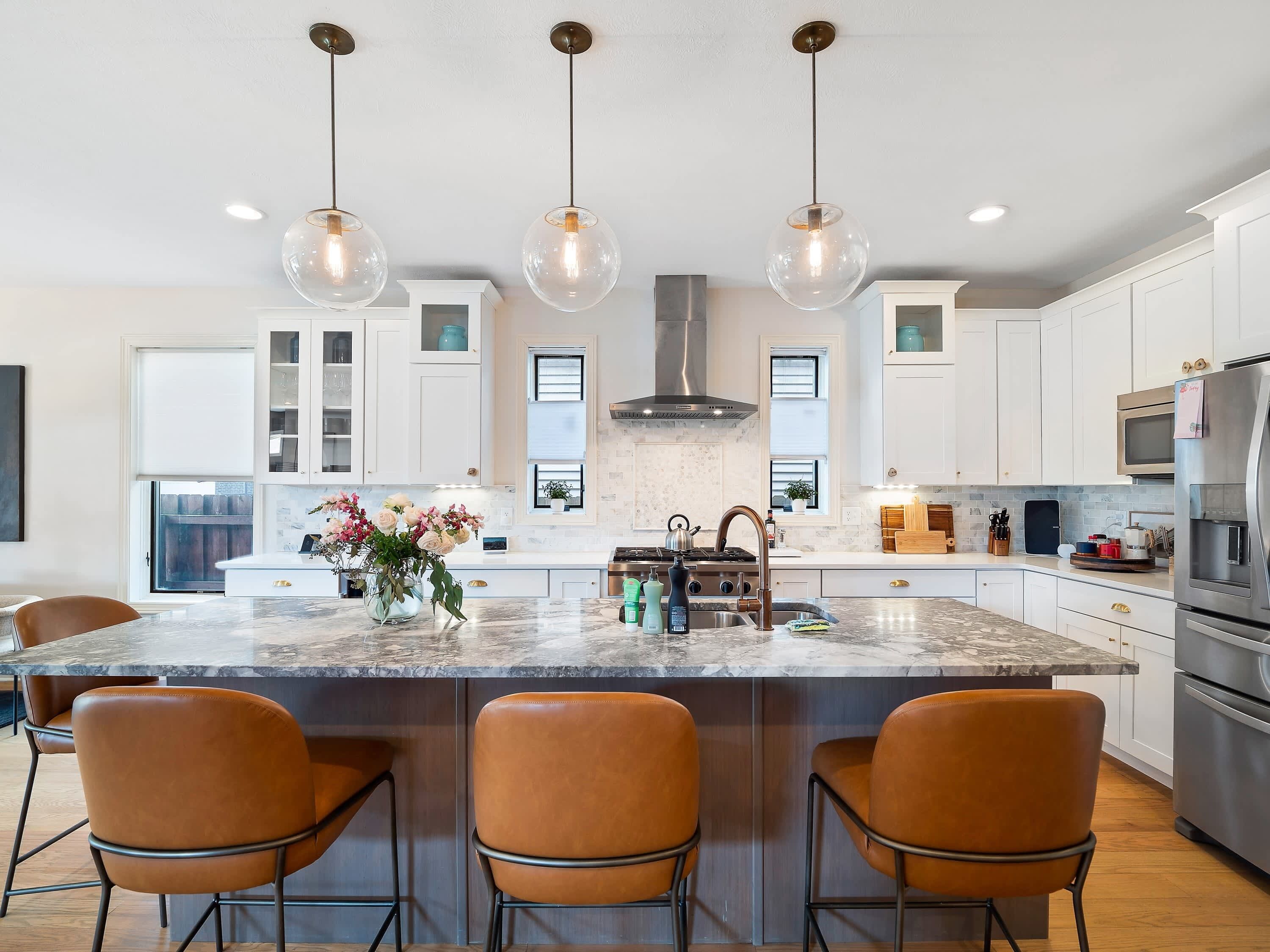 Una cocina moderna con una isla central, luces colgantes y electrodomésticos de acero inoxidable.