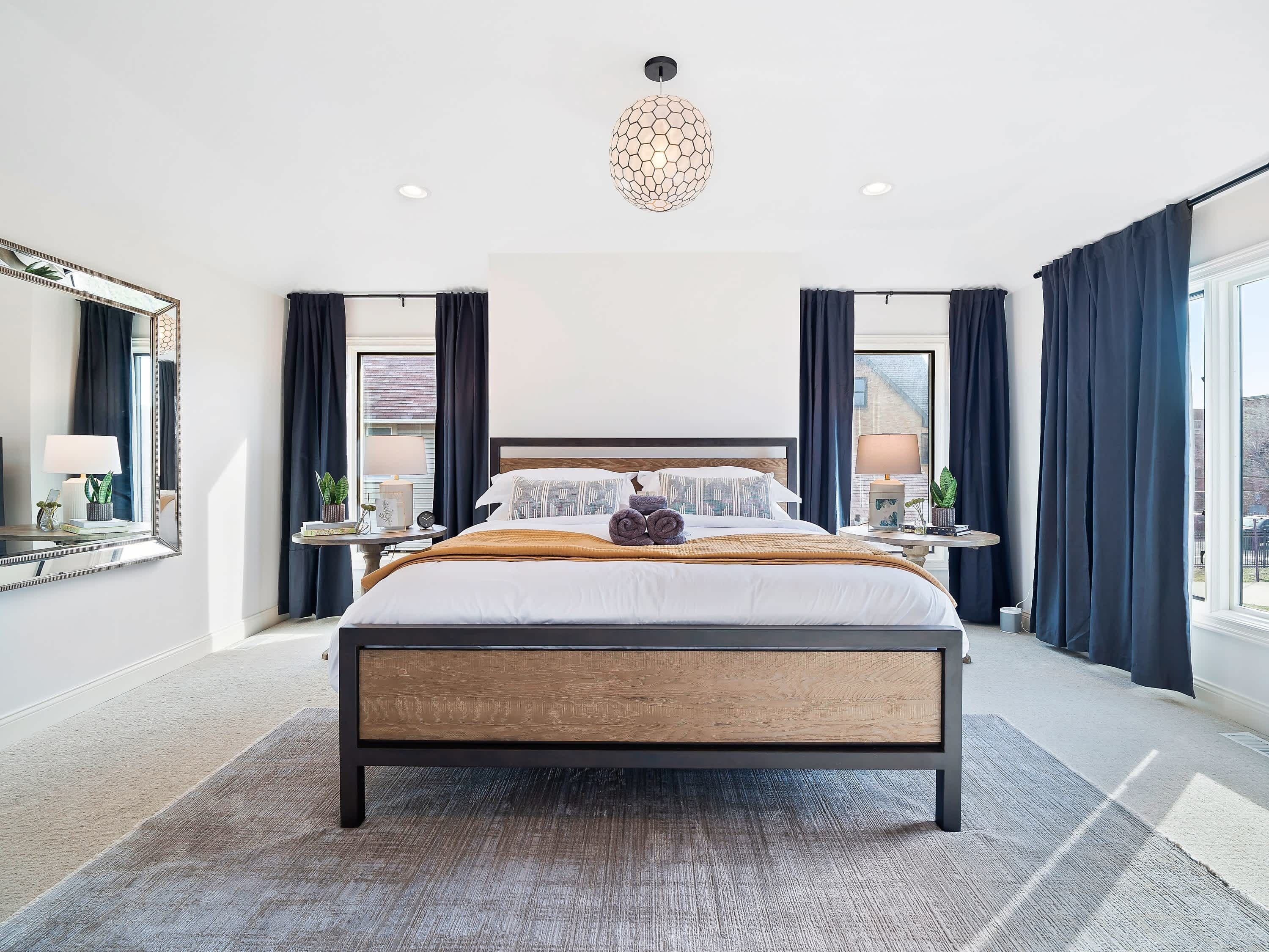 Un dormitorio moderno con una cama grande, mesitas de noche, un espejo y vistas a la ciudad.