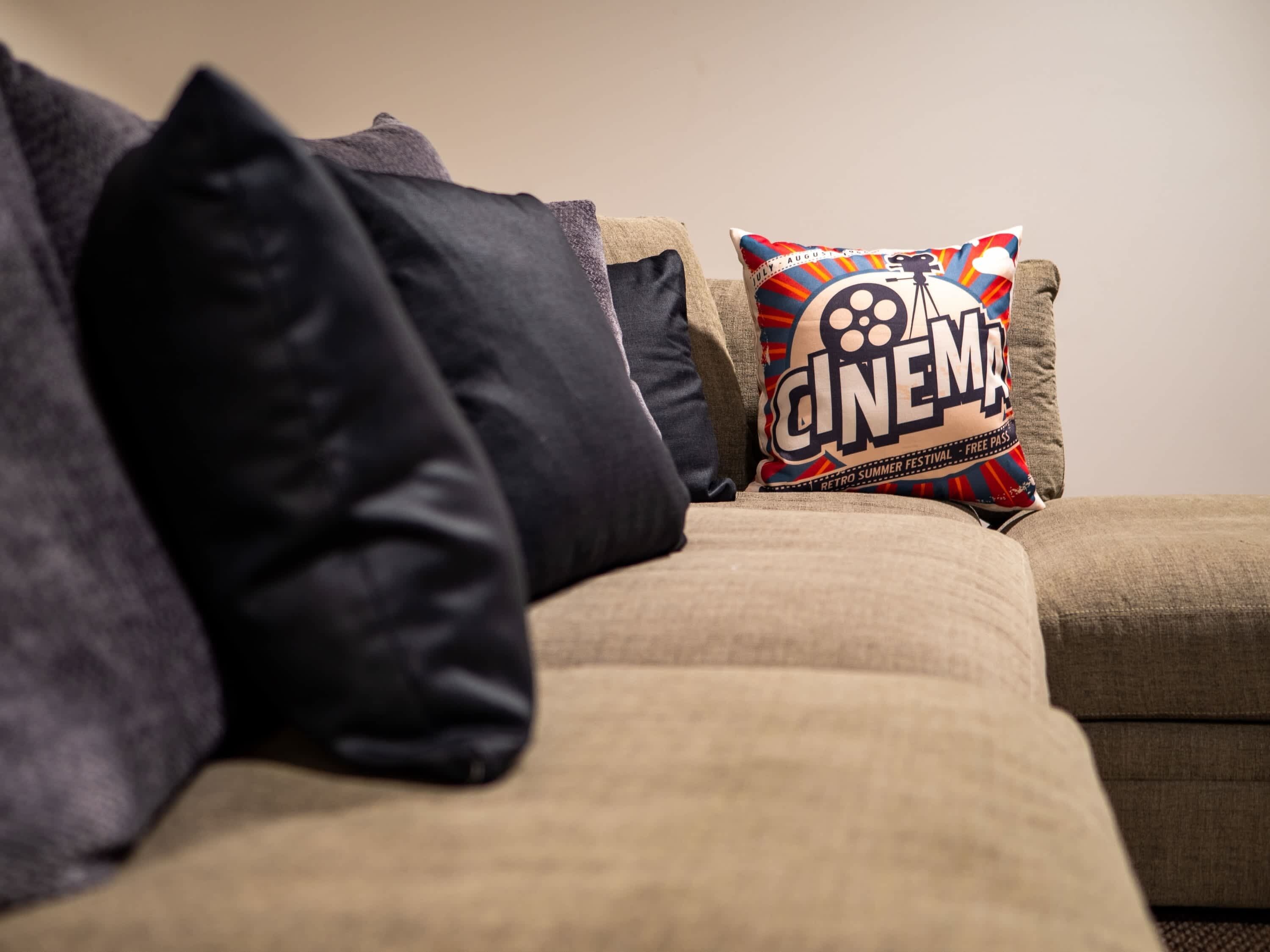 A beige sofa with multiple pillows, including a colorful one with 'CINEMA' text.