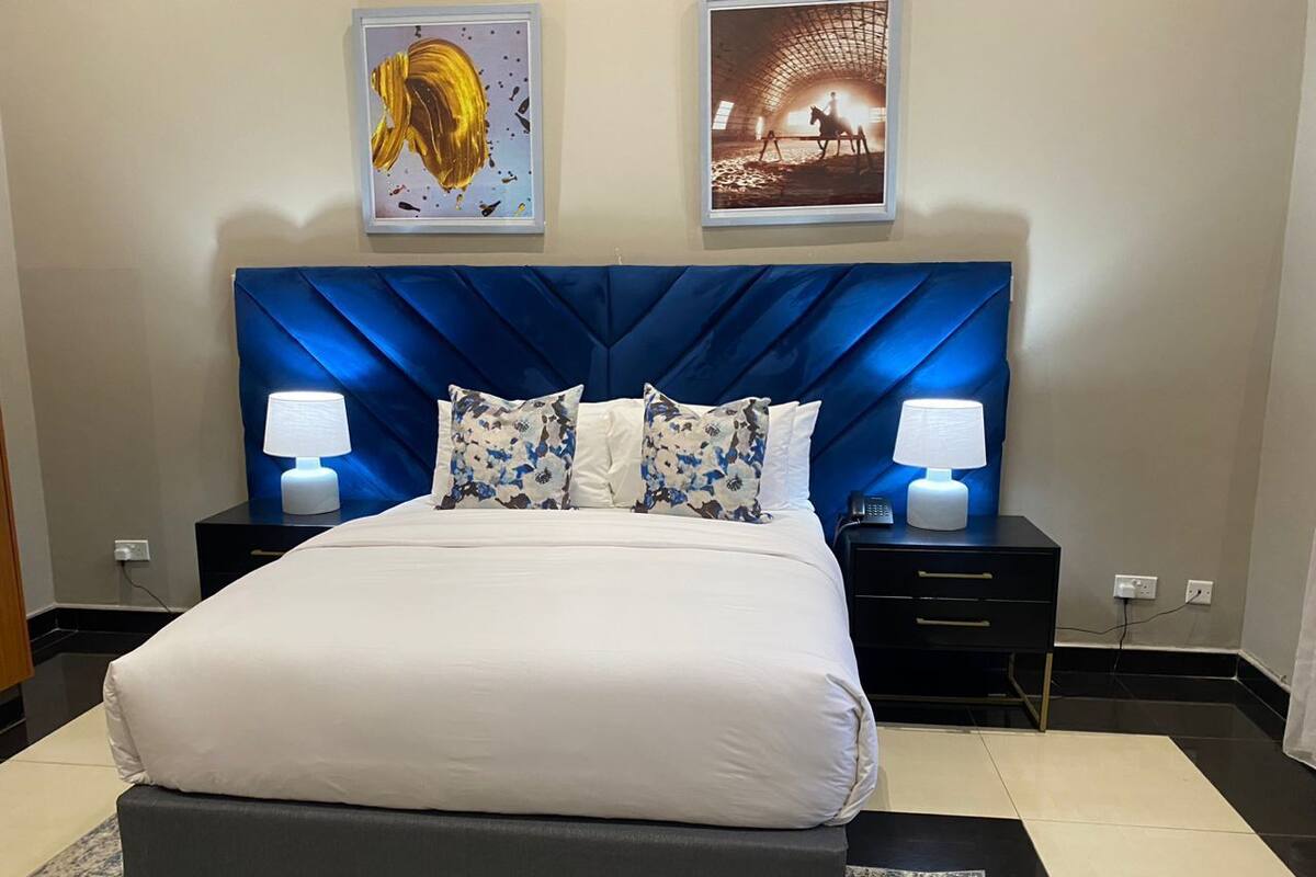A bedroom with a large bed, two nightstands, a blue headboard, and two framed pictures on the wall.