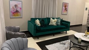 A modern living room with a green sofa, two armchairs, a coffee table, and artwork on the walls. - Topaz Villas (Lilongwe)