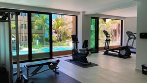 Et moderne fitnesscenter med træningsudstyr, store vinduer og udsigt til en swimmingpool.