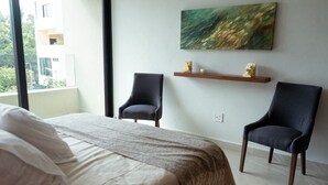 Et hotelværelse med en seng, to lænestole, en træhylde med pynteting og et maleri på væggen.