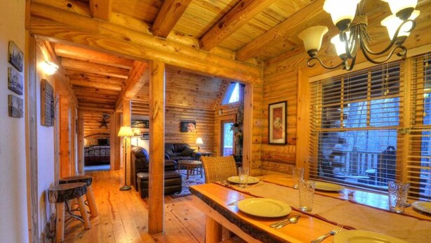 A wooden cabin interior with a dining area, a sofa, and a fireplace.