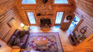 A cozy cabin interior with a stone fireplace, leather sofa, and a large rug.