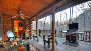 A wooden deck with a grill, chairs, and a fireplace.