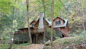 A cabin with a stone chimney, wooden deck, and a view of the forest.