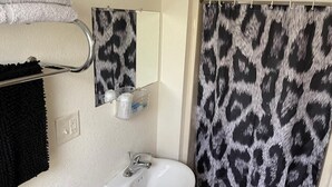 Ein Badezimmer mit einem weißen Waschbecken, einem Spiegel und einer Duschvorhang mit Leopardenmuster.