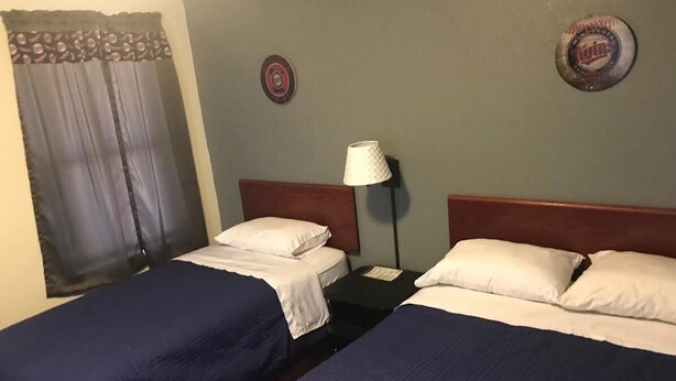 Ein Hotelzimmer mit zwei Einzelbetten, einem Nachttisch, einer Lampe und einer Wanduhr.