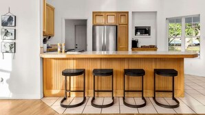 A modern kitchen with a central island, wooden bar stools, stainless steel appliances, and a view of the outdoors. - Canyon Cottage - 1 Acre w/Fire Pits & Game Room! (Canyon Lake)