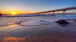 A beach with a pier extending into the water, waves gently lapping at the shore, and the sun setting in the background. - 7BD Family, Event Friendly 5min 2 Beach, Boardwalk (San Diego)