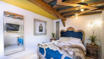 A bedroom with a large bed, a mirror, a framed picture, and a wooden ceiling.