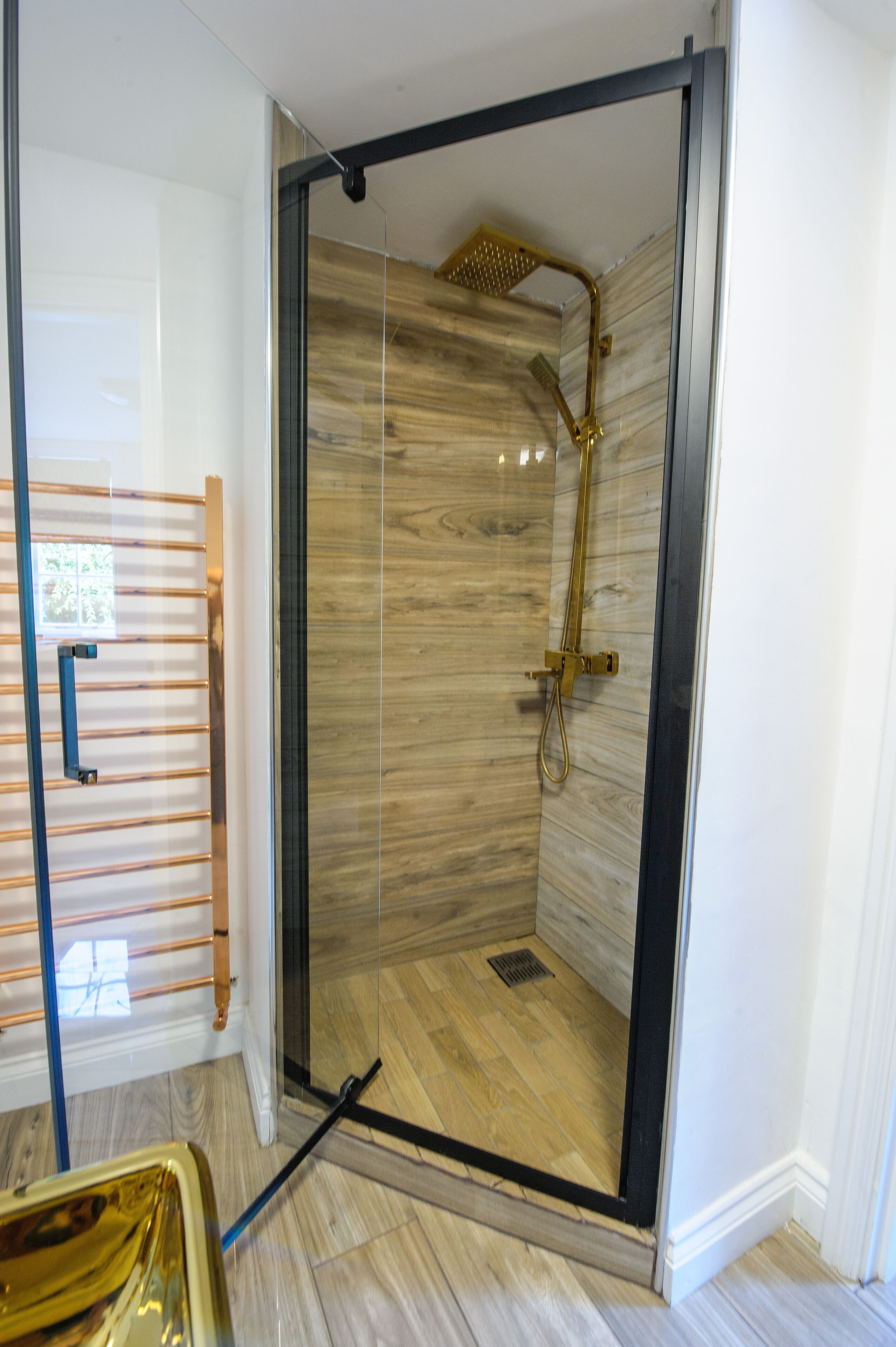 A glass-enclosed shower with a wooden interior, a metal showerhead, and a handheld shower attachment.
