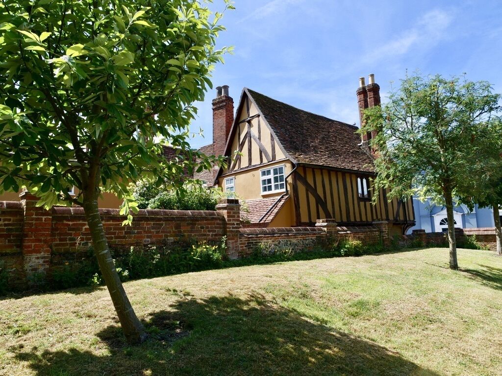 A traditional Tudor-style house with a brick wall, a thatched roof, and chimneys.