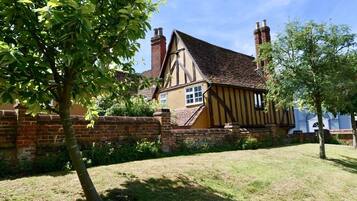 A traditional Tudor-style house with a brick wall, a thatched roof, and chimneys.