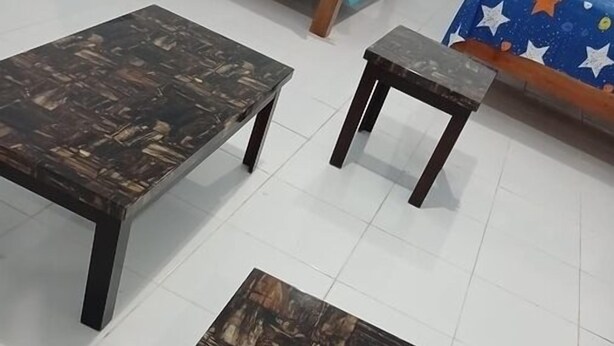 Quarto com uma cama coberta por um cobertor azul, duas mesas quadradas com estrutura de madeira escura e tampos de vidro, e uma pequena mesa com tampo de madeira escura e pés.