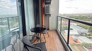 A balcony with a glass railing, a round table with two chairs, and an air conditioning unit.