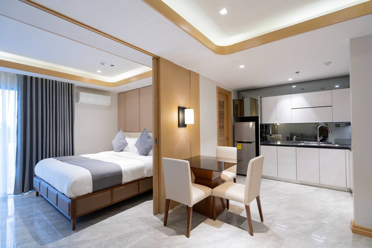 Ein modernes Hotelzimmer mit Bett, Esstisch mit Stühlen, Küchenzeile und Bad.