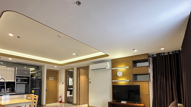 A modern living room with a sofa, a coffee table, and a TV area. There is a kitchen in the background with a dining area.