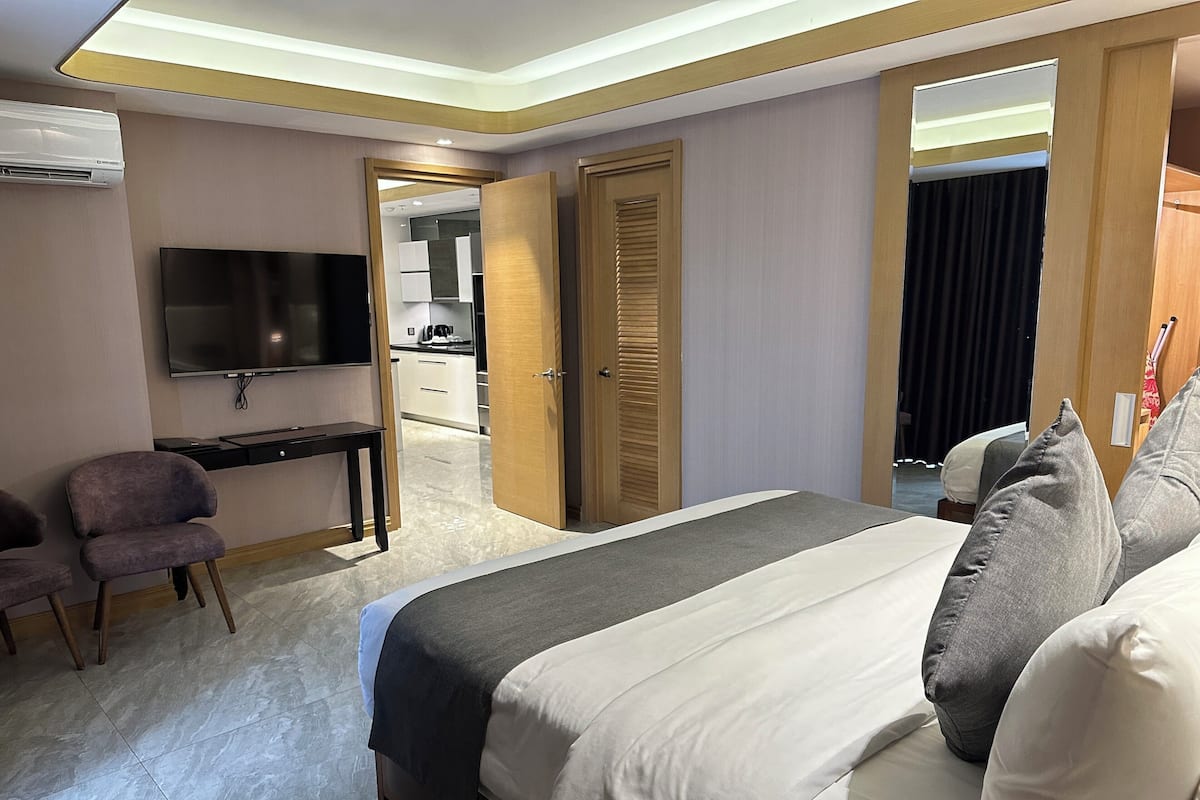 Ein Hotelzimmer mit Bett, Schreibtisch, Stuhl, Fernseher und Blick zur Küche.