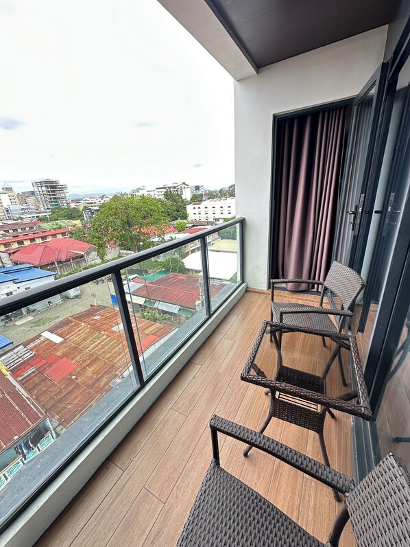 A balcony with wicker chairs, a glass railing, and a view of buildings and a construction site. - One Euphoria Luxe Hotel (Angeles City)