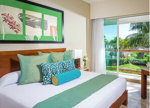 Relax in a serene room with a large bed, framed artwork, and a view of lush green surroundings.