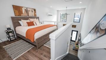 A bedroom with a wooden bed, white walls, and a staircase leading to a loft area.