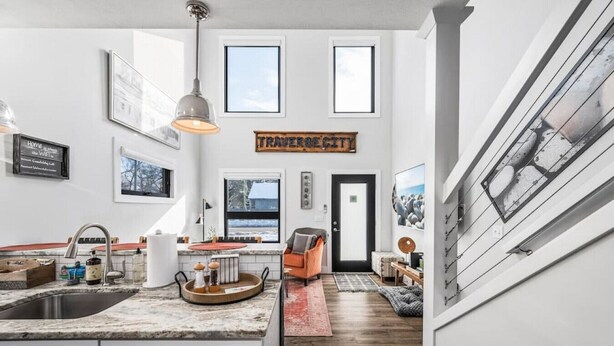 A modern kitchen with a large island, a dining area with a red rug, and a sign reading "TRAVEL CITY" on the wall.