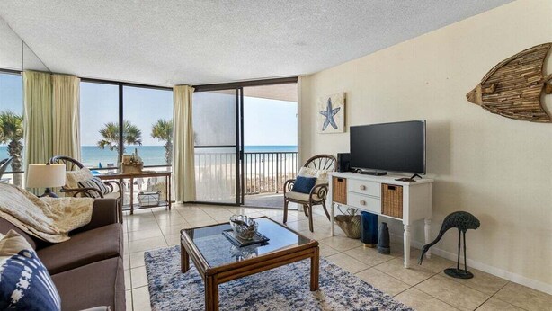 Habitación con sofá, mesa de centro, televisor y balcón con vista al océano.