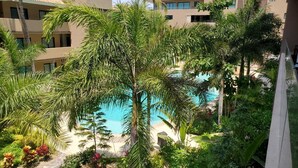 A pool surrounded by lush greenery and palm trees, with modern buildings in the background. - Villa Dahlia, Luxury Studio, steps from the beach! (San Francisco)