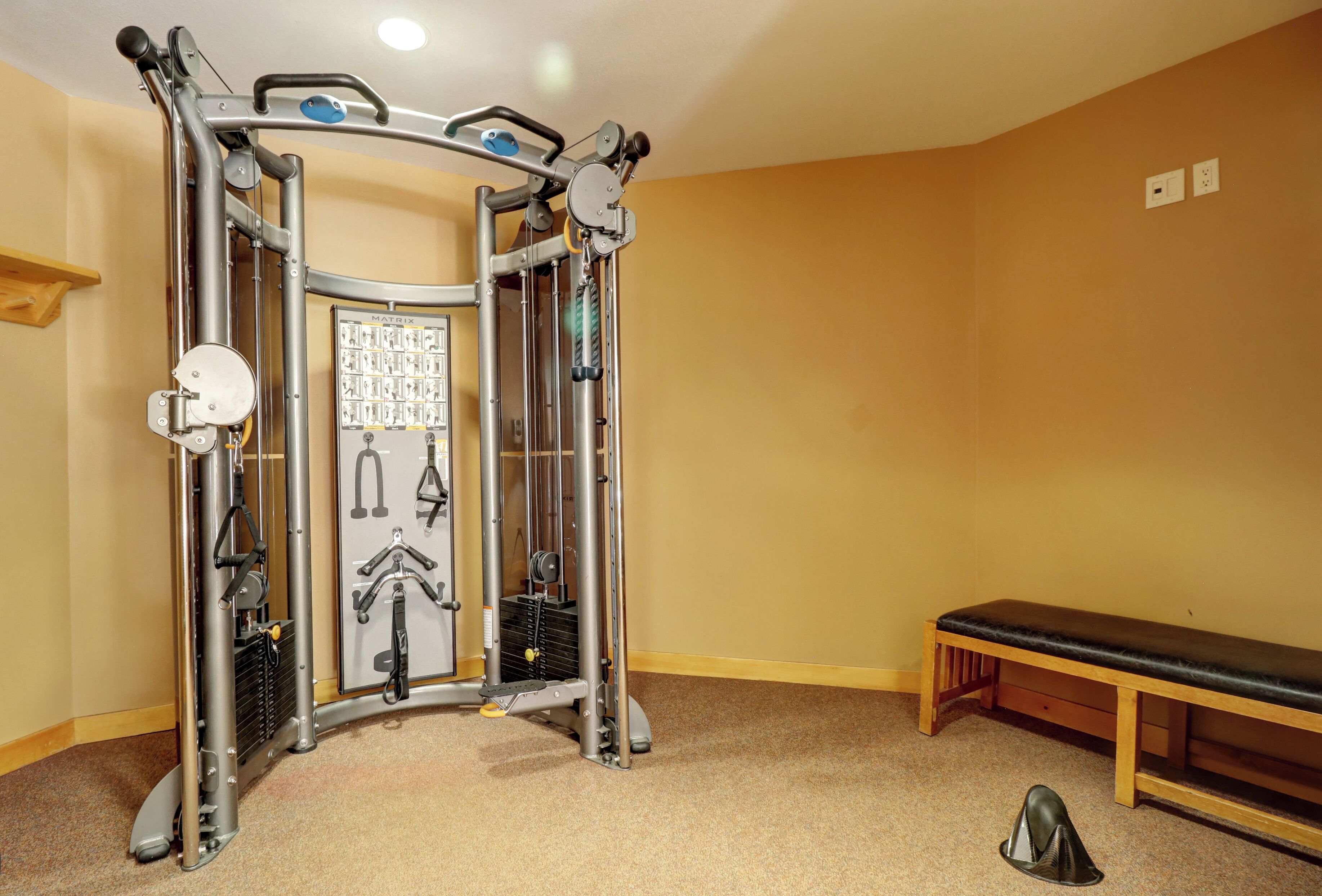A gym with a pull-up bar system, a bench, and a wall-mounted control panel.