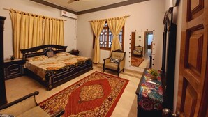 A bedroom with a bed, a chair, a table, a ceiling fan, and a window with curtains. - 6 - 8 Guests 3 Bedrooms 3 Beds 4 Baths. (Karachi)