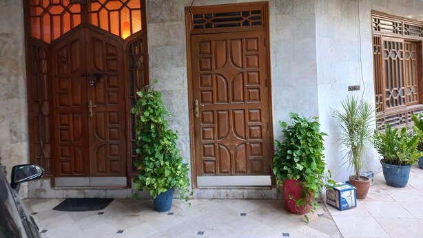 A building entrance with two wooden doors, potted plants, and a tiled floor. - 6 - 8 Guests 3 Bedrooms 3 Beds 4 Baths. (Karachi)