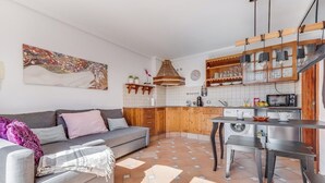 A modern living room with a grey sofa, a coffee table, and a kitchen area with wooden cabinets and a tiled backsplash. - Home2Book Charming Attic El Rincón de Telde, BBQ (Telde)
