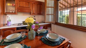 A kitchen with wooden cabinets, a dining table set with plates and glasses, and a window with a view of greenery. - Vacation home Salvia by Interhome (Massa Marittima)