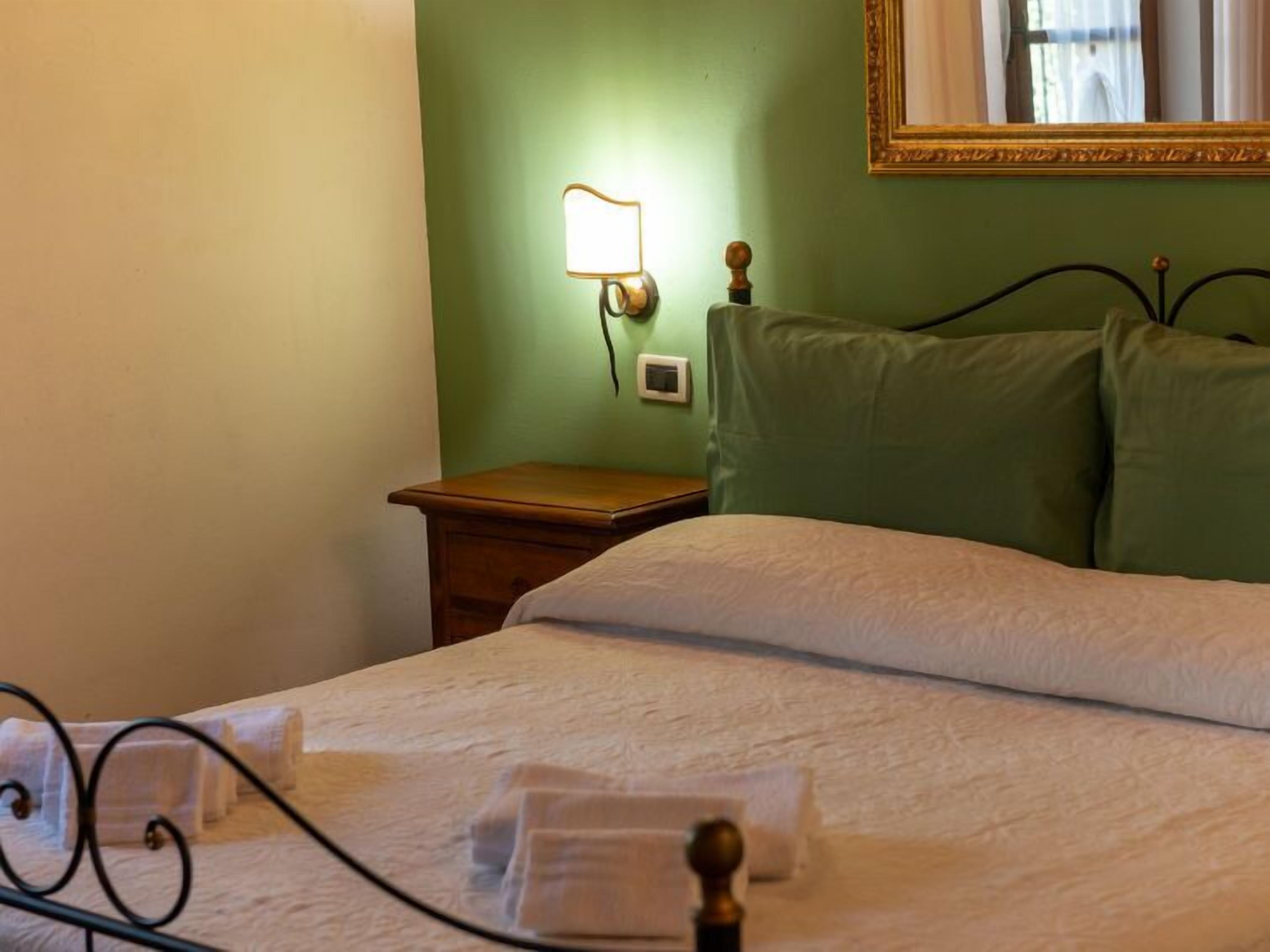 A neatly made bed with white linens, a bedside table with a lamp, and a green wall with a mirror.