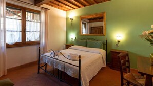 A bedroom with a bed, a wooden ceiling, a window with curtains, a mirror, and a bedside table with a lamp. - Vacation home Salvia by Interhome (Massa Marittima)