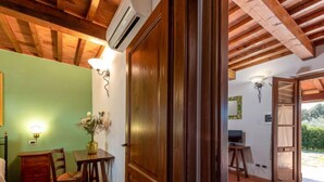 A room with a wooden ceiling, a green wall, a wooden door, a table with a vase of flowers, a chair, and a red sofa. - Vacation home Salvia by Interhome (Massa Marittima)