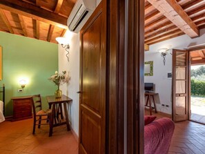A room with a wooden ceiling, a green wall, a wooden door, a table with a vase of flowers, a chair, and a red sofa.